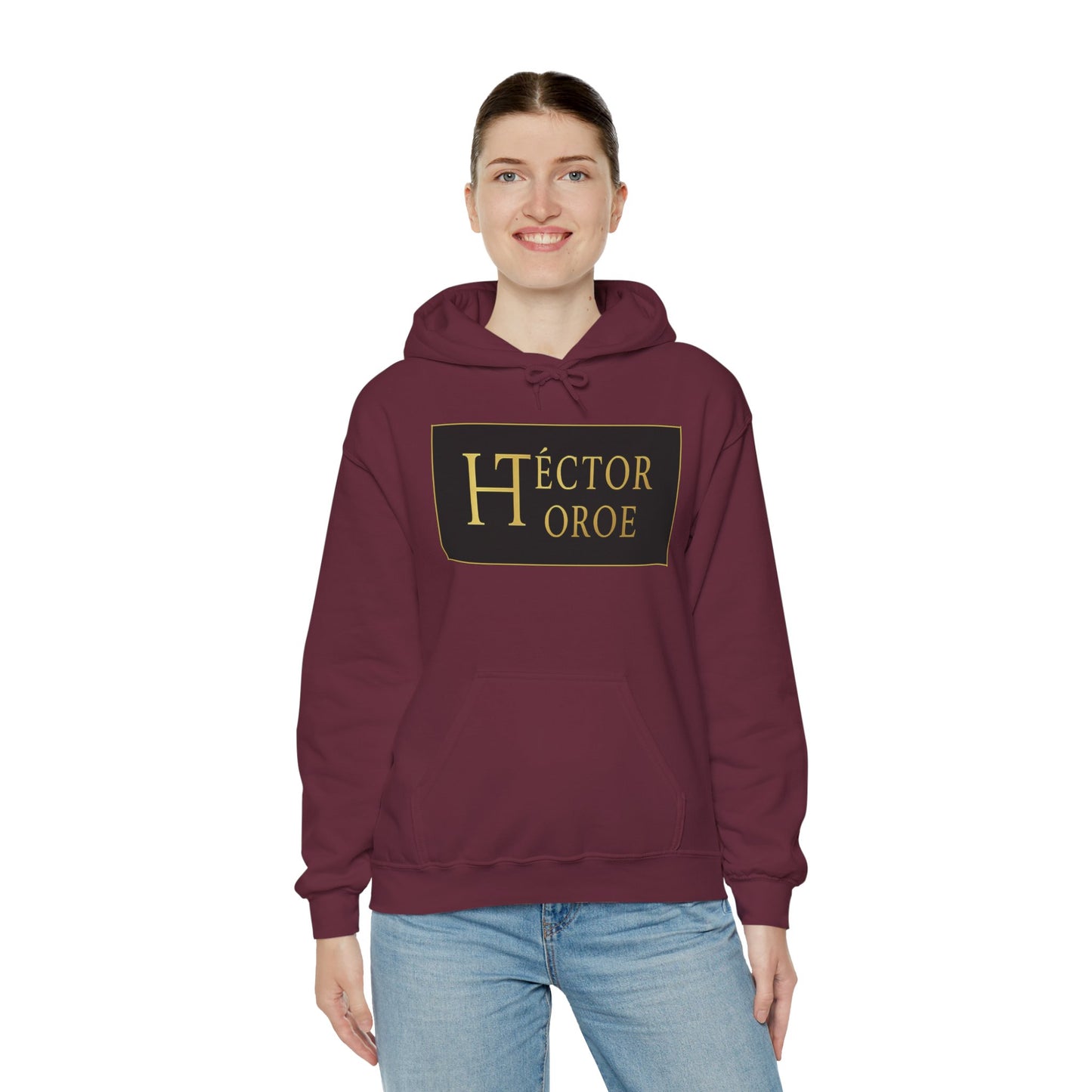 una mujer con sudadera maroon con capucha y bolsillo frontal, con un logotipo rectangular negro y dorado en el centro que muestra el texto “Héctor Toroe”. 