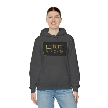 una mujer con sudadera brezo oscuro con capucha y bolsillo frontal, con un logotipo rectangular negro y dorado en el centro que muestra el texto “Héctor Toroe”.
