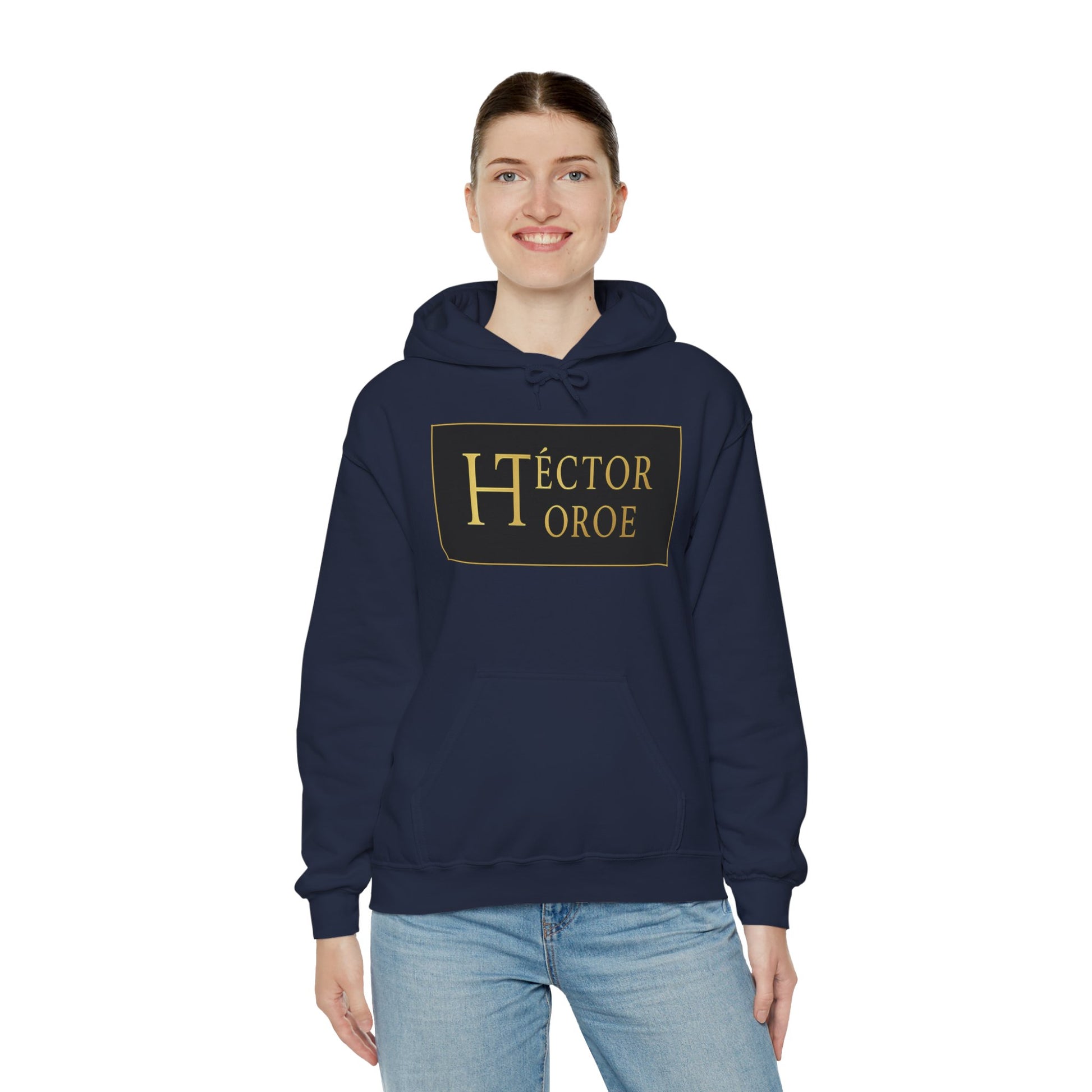 una mujer con sudadera azul marino con capucha y bolsillo frontal, con un logotipo rectangular negro y dorado en el centro que muestra el texto “Héctor Toroe”. 