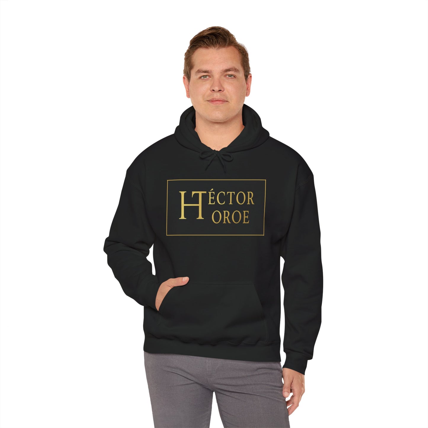 un hombre con sudadera negro con capucha y bolsillo frontal, con un logotipo rectangular negro y dorado en el centro que muestra el texto “Héctor Toroe”.