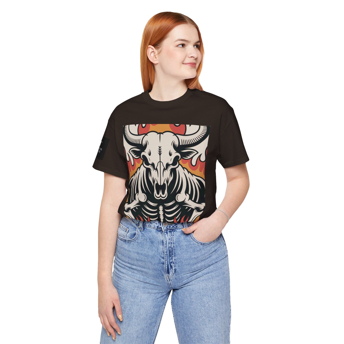 Mujer usando una camiseta cafe de manga corta con un diseño gráfico central de una calavera de toro con cuernos, estilo ilustración, sobre un fondo de llamas en tonos rojo, naranja y negro.