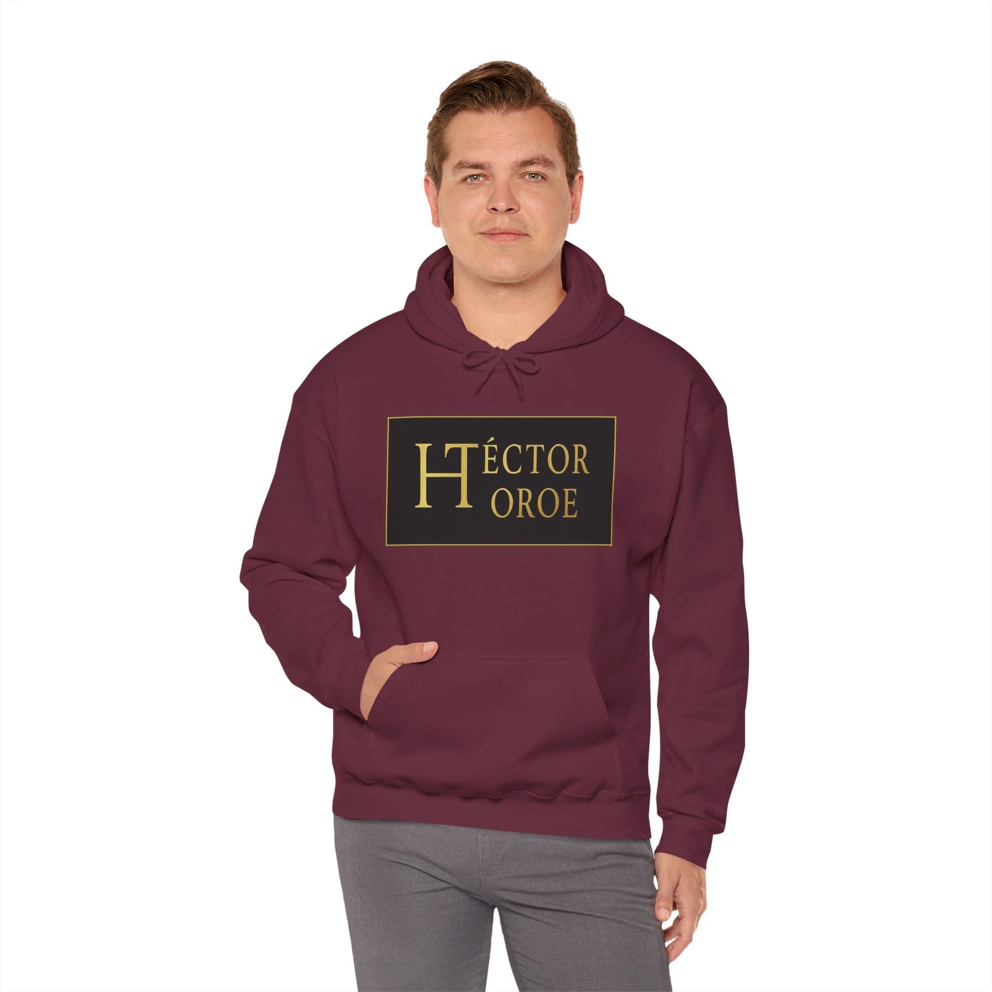 un hombre con sudadera maroon con capucha y bolsillo frontal, con un logotipo rectangular negro y dorado en el centro que muestra el texto “Héctor Toroe”.