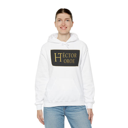 una mujer con sudadera blanca con capucha y bolsillo frontal, con un logotipo rectangular negro y dorado en el centro que muestra el texto “Héctor Toroe”. 