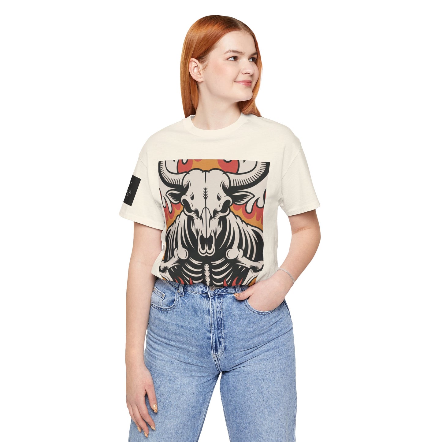 Mujer usando una camiseta natural de manga corta con un diseño gráfico central de una calavera de toro con cuernos, estilo ilustración, sobre un fondo de llamas en tonos rojo, naranja y negro.