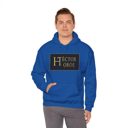 un hombre con sudadera royal con capucha y bolsillo frontal, con un logotipo rectangular negro y dorado en el centro que muestra el texto “Héctor Toroe”.