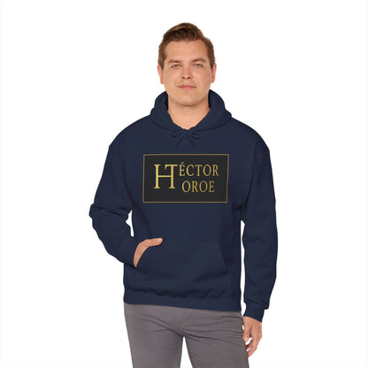 un hombre con sudadera azul marino con capucha y bolsillo frontal, con un logotipo rectangular negro y dorado en el centro que muestra el texto “Héctor Toroe”.
