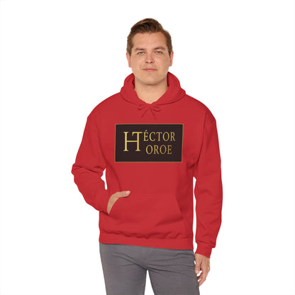 un hombre con sudadera rojo con capucha y bolsillo frontal, con un logotipo rectangular negro y dorado en el centro que muestra el texto “Héctor Toroe”.
