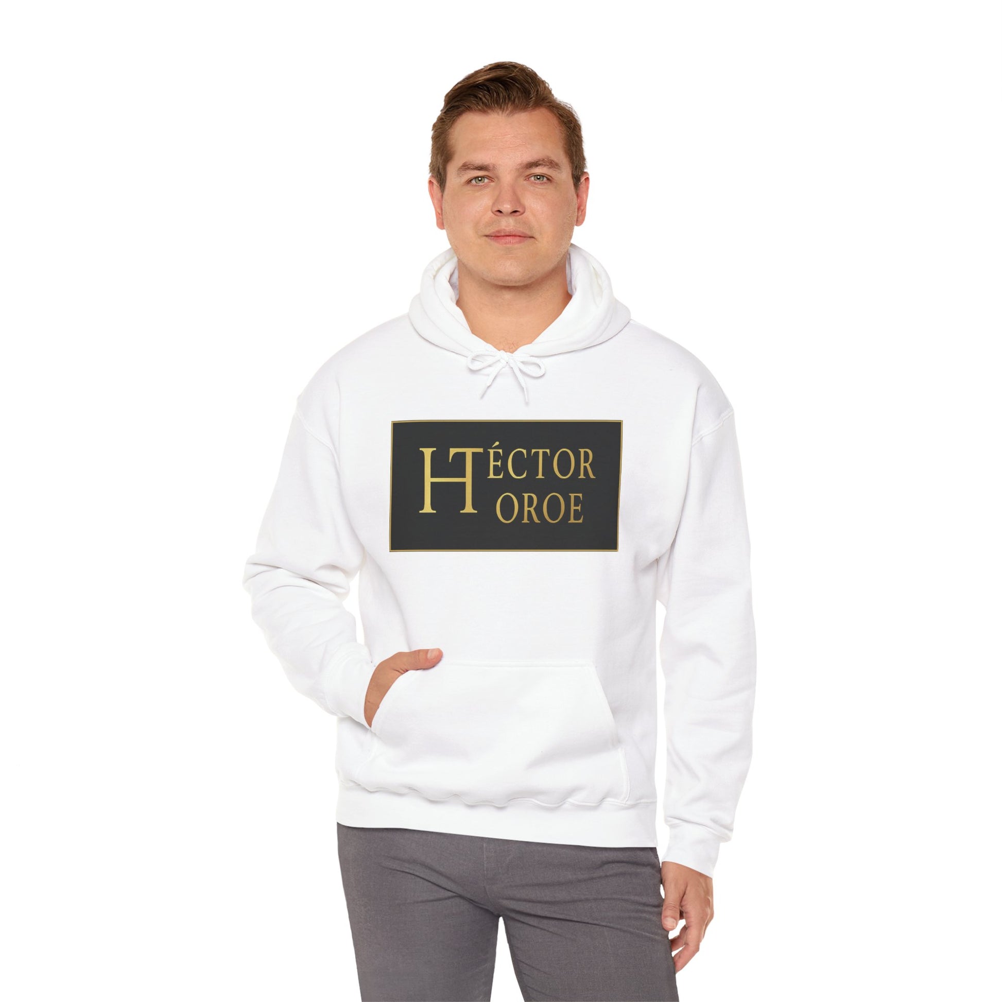 un hombre con sudadera blanca con capucha y bolsillo frontal, con un logotipo rectangular negro y dorado en el centro que muestra el texto “Héctor Toroe”.